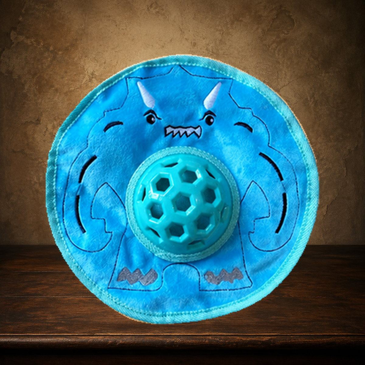 The Little Monster Disc — Crinkle & Squeak Toy displayed on the approved antique plaster and walnut table